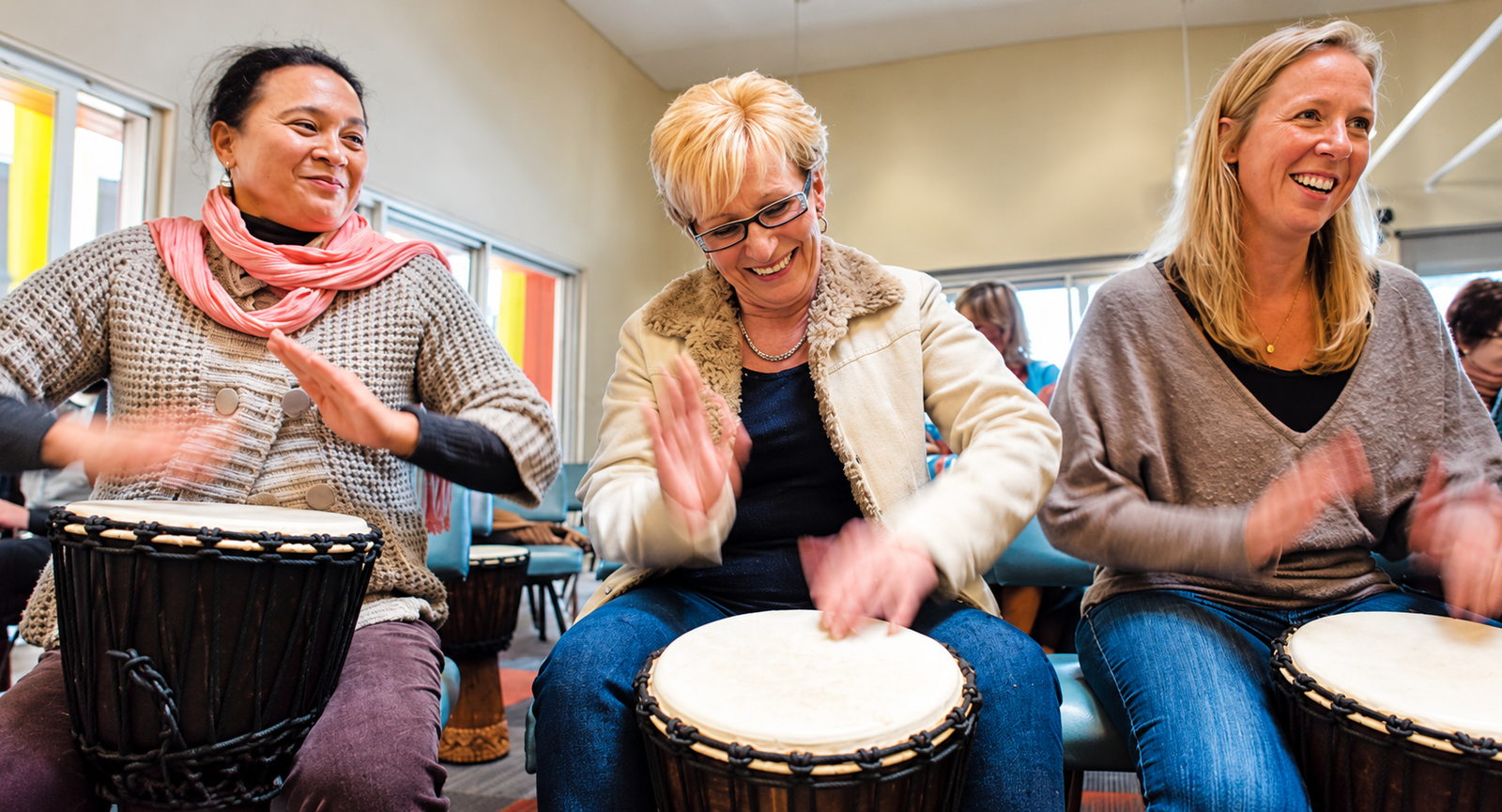 Three participants smiling and playing djembes together during an InRhythm drumming session